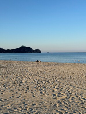 A sandy beach with footprints, a calm sea, and a distant rocky outcrop.