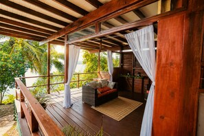 A wooden deck with a cushioned seating area, a view of greenery, and a wooden railing. - Ocean Views & 2 Private Pools || Blue Dolphin Villa (Fort Jeudy)