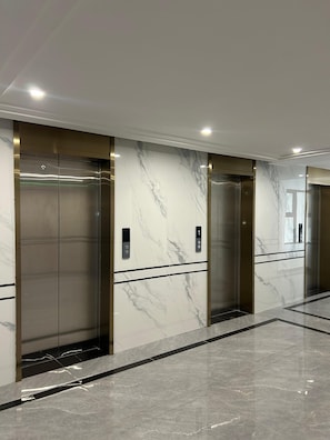 A modern elevator with a metallic finish and marble wall panels. - Traveler's Loft- Park views near JKIA&SGR with Pool & Gym (Nairobi)