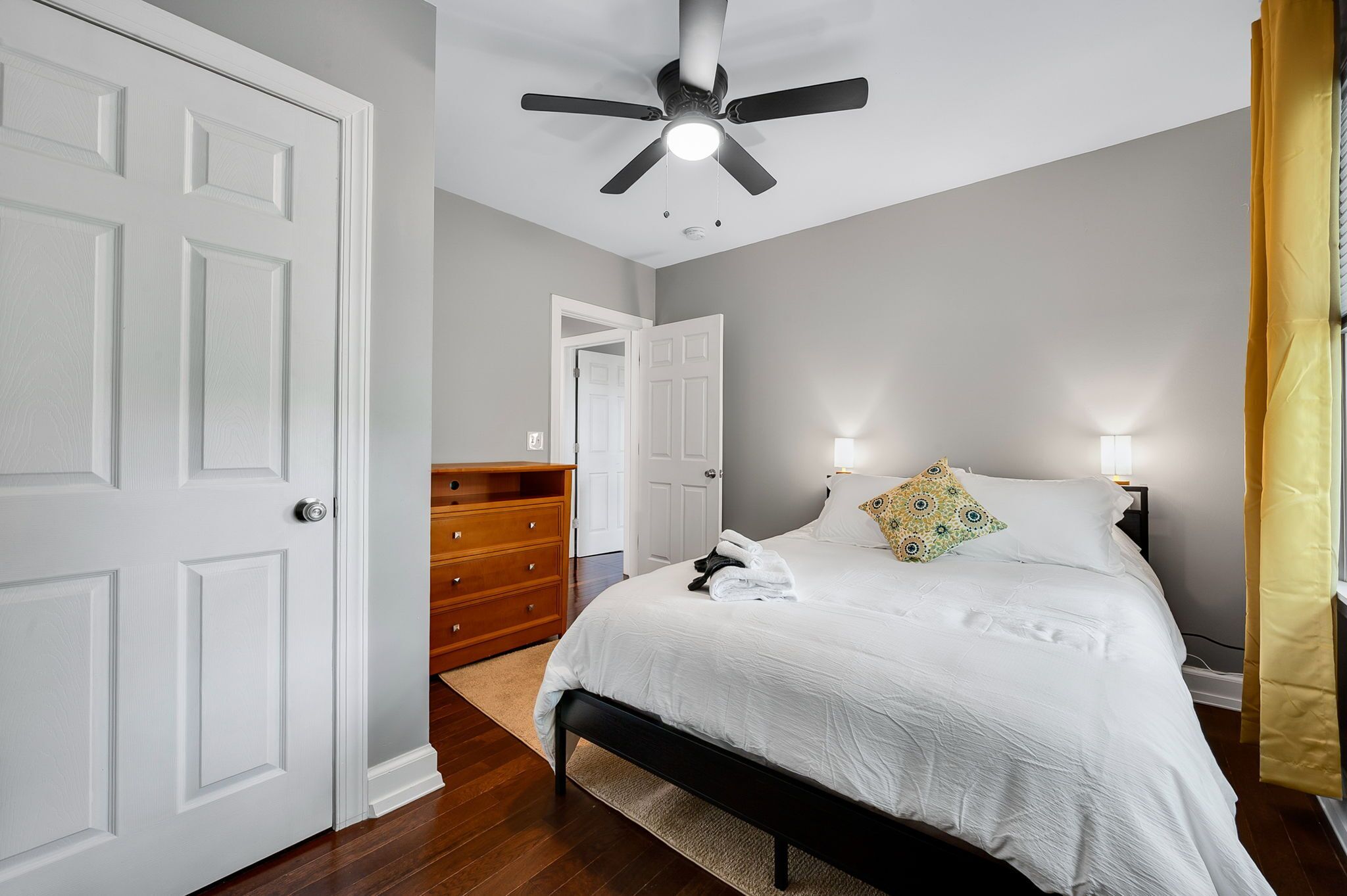A bedroom with a bed, a wooden dresser, a ceiling fan, and a door.