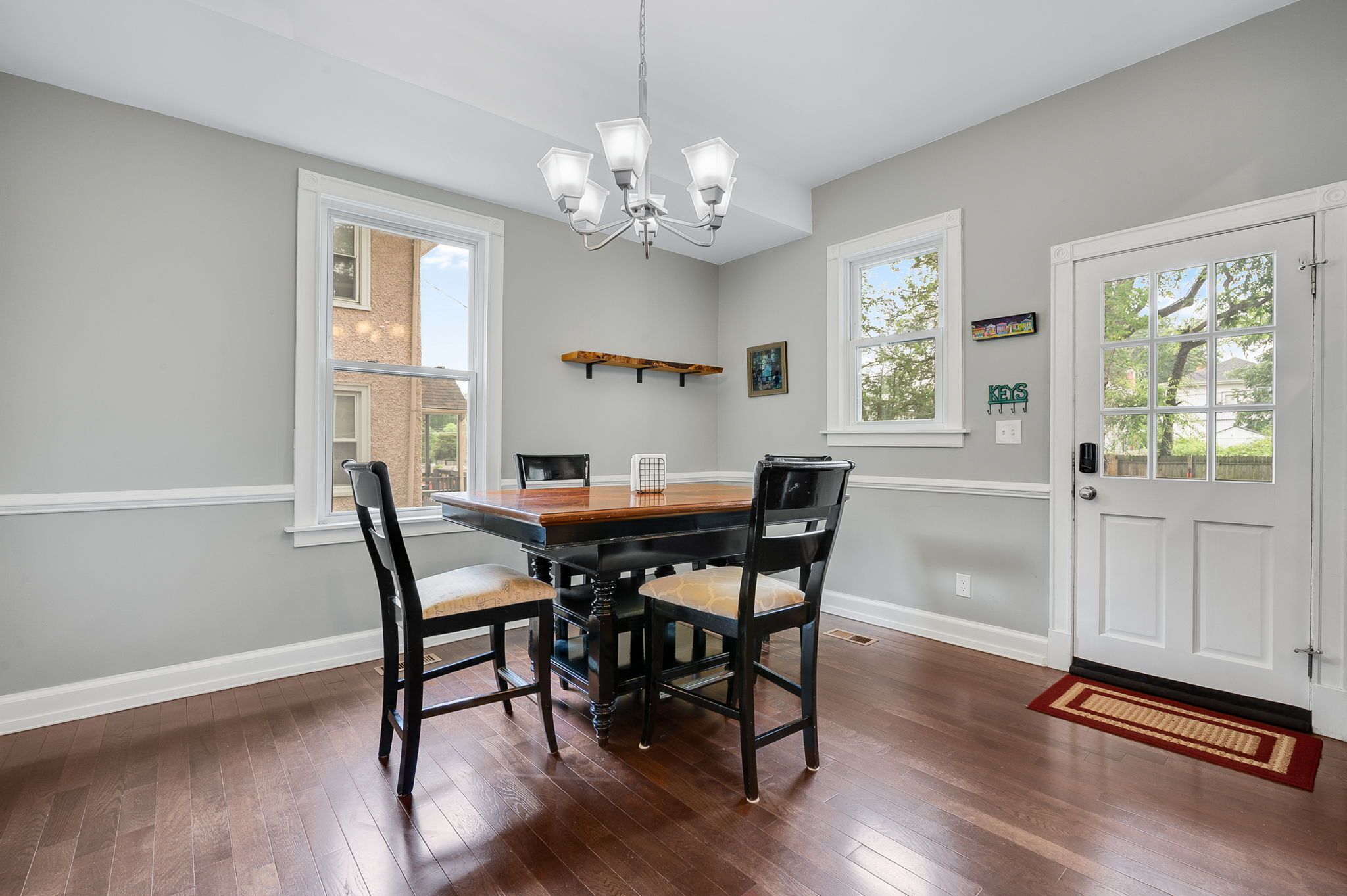 A dining room with a wooden table and chairs, a chandelier, and a door with a window.