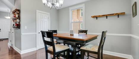 A dining room with a wooden table and chairs, a chandelier, and a window with a view.