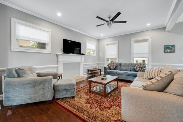 A living room with a fireplace, a ceiling fan, and a television.