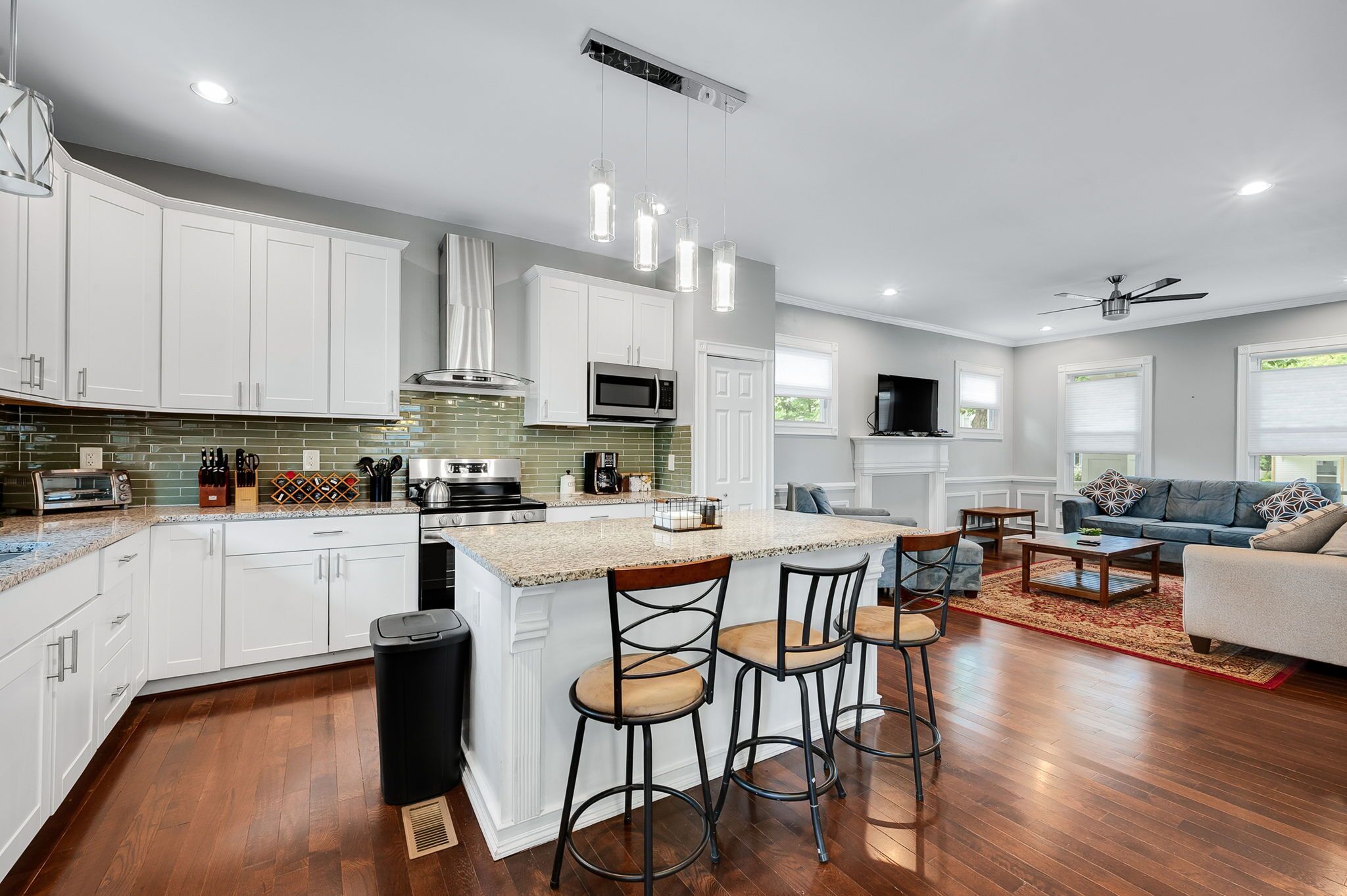 A modern kitchen with white cabinets, a central island with bar stools, and a dining area with a sofa and coffee table.