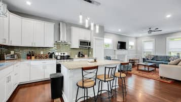 A modern kitchen with white cabinets, a central island with bar stools, and a dining area with a sofa and coffee table.