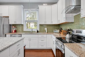 A modern kitchen with white cabinets, a granite countertop, a stainless steel range, and a window with blinds. - Spacious 3 BR Home with Fire Pit & Fenced Backyard - Pet Friendly (Richmond)