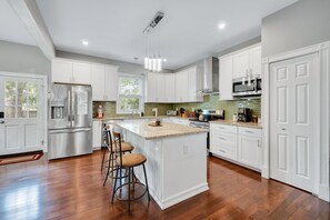 A modern kitchen with white cabinetry, stainless steel appliances, and a central island with stools.