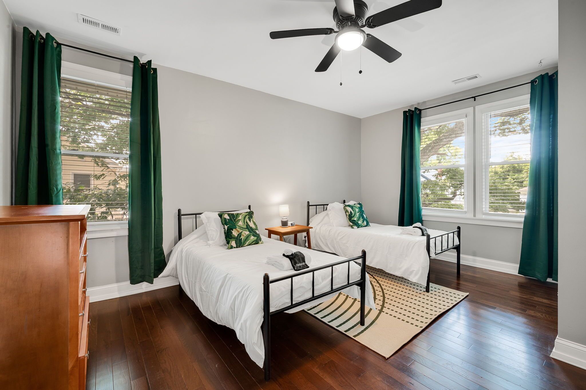 A bedroom with two beds, a ceiling fan, a nightstand with a lamp, and a window with curtains.