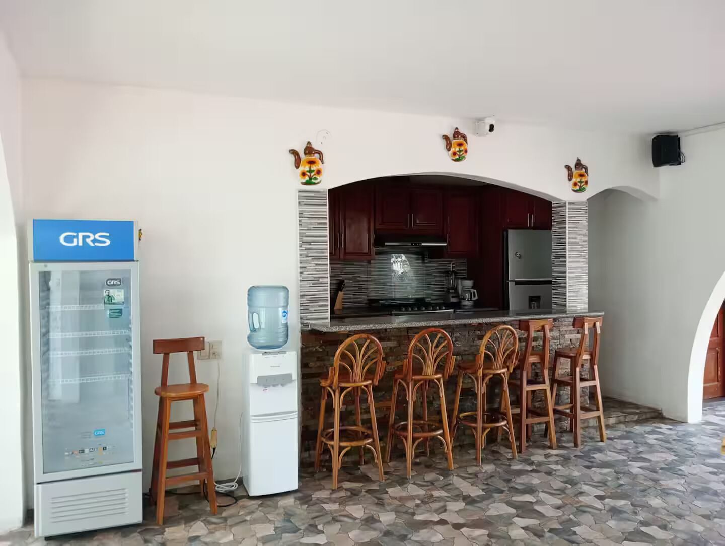 Eine Küche mit Wasserspender, Kühlschrank und einer Bar inklusive Stühlen.