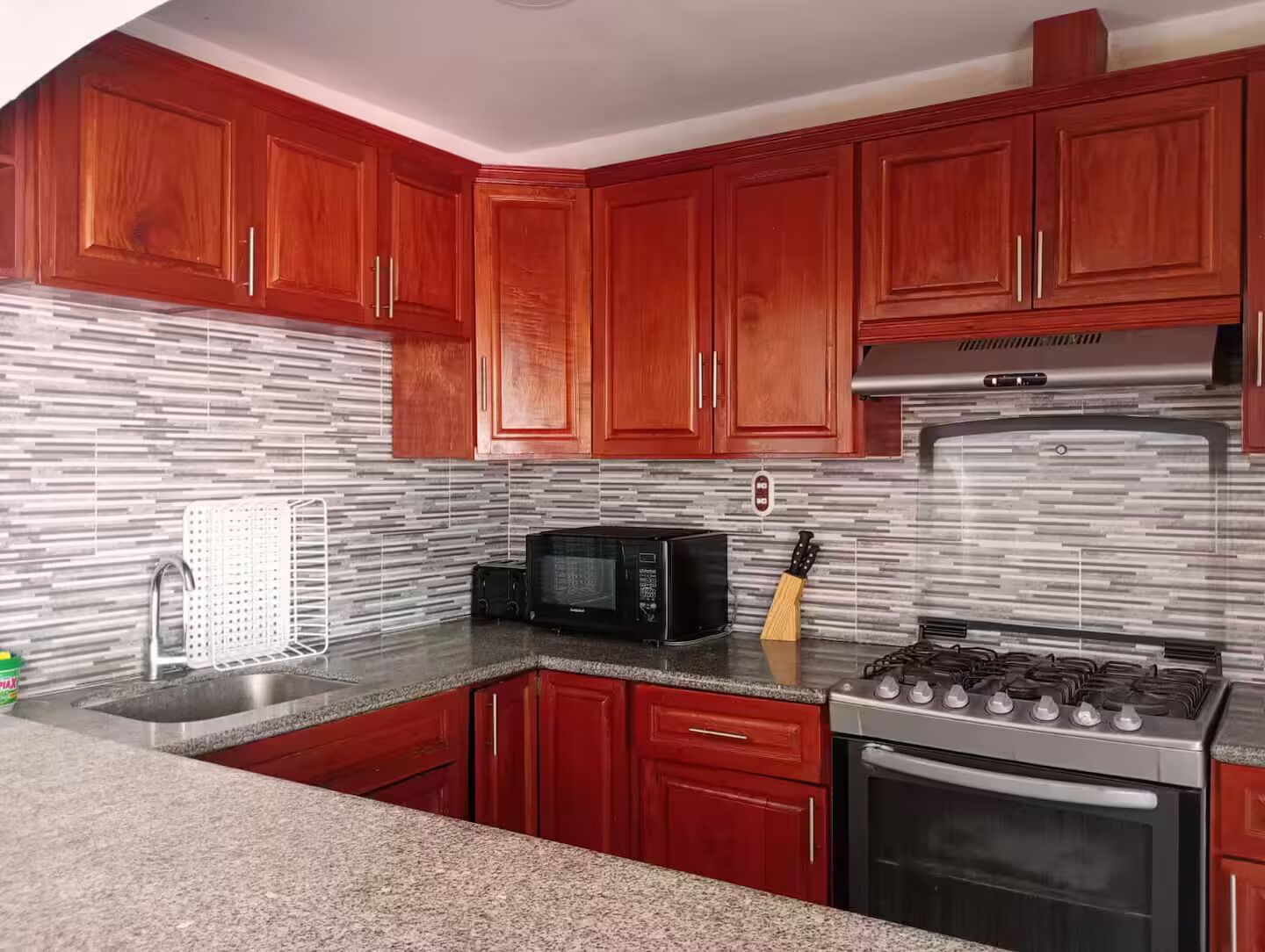 A kitchen with red cabinets, a stainless steel range hood, a microwave, and a gas stove.