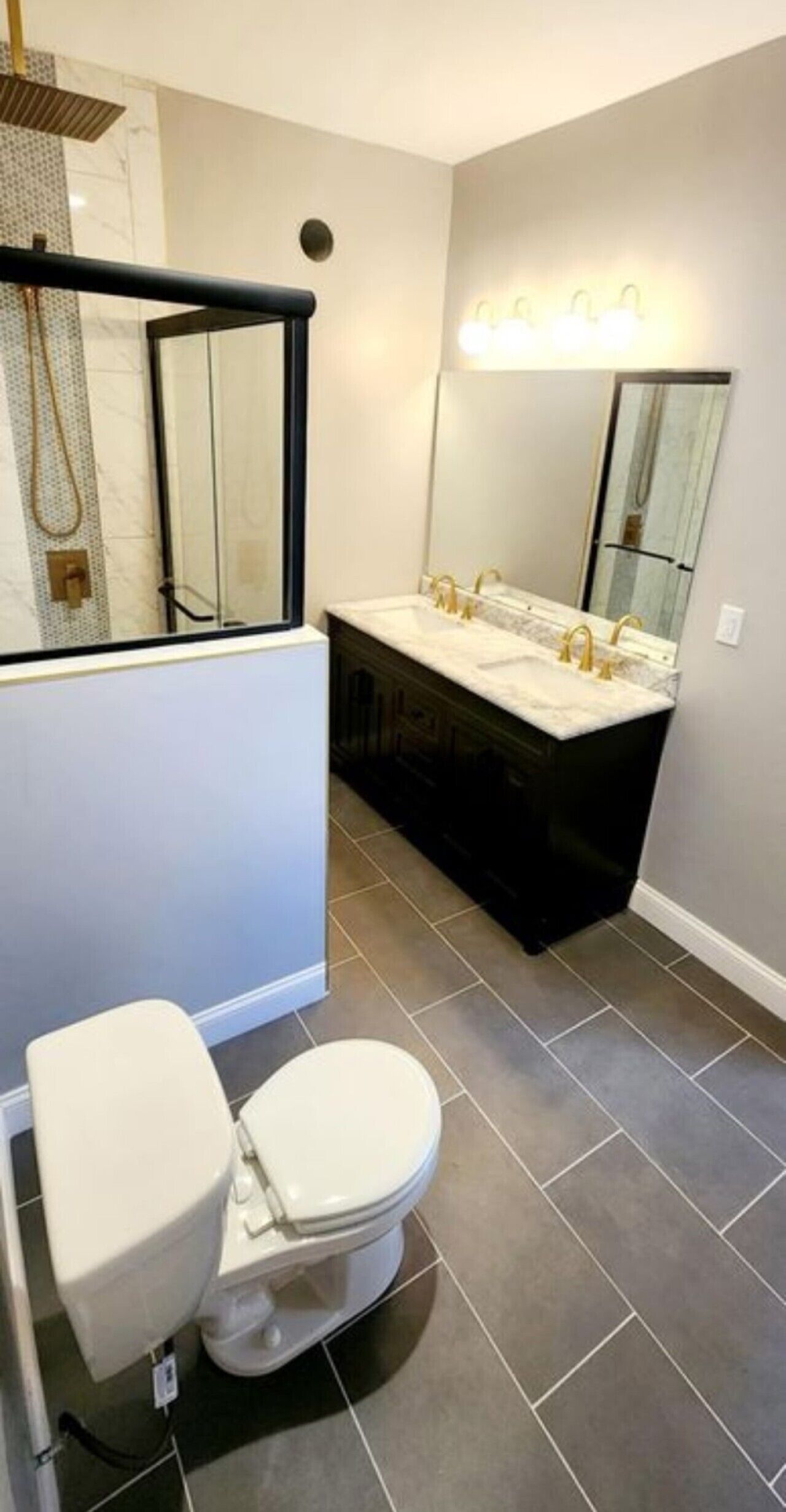 A modern bathroom with a toilet, a vanity with a mirror, and a shower area.