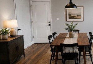 A dining area with a wooden table, black chairs, a lamp, and a framed picture on the wall. - Centrally Located Cozy Downtown Home (Kansas City)