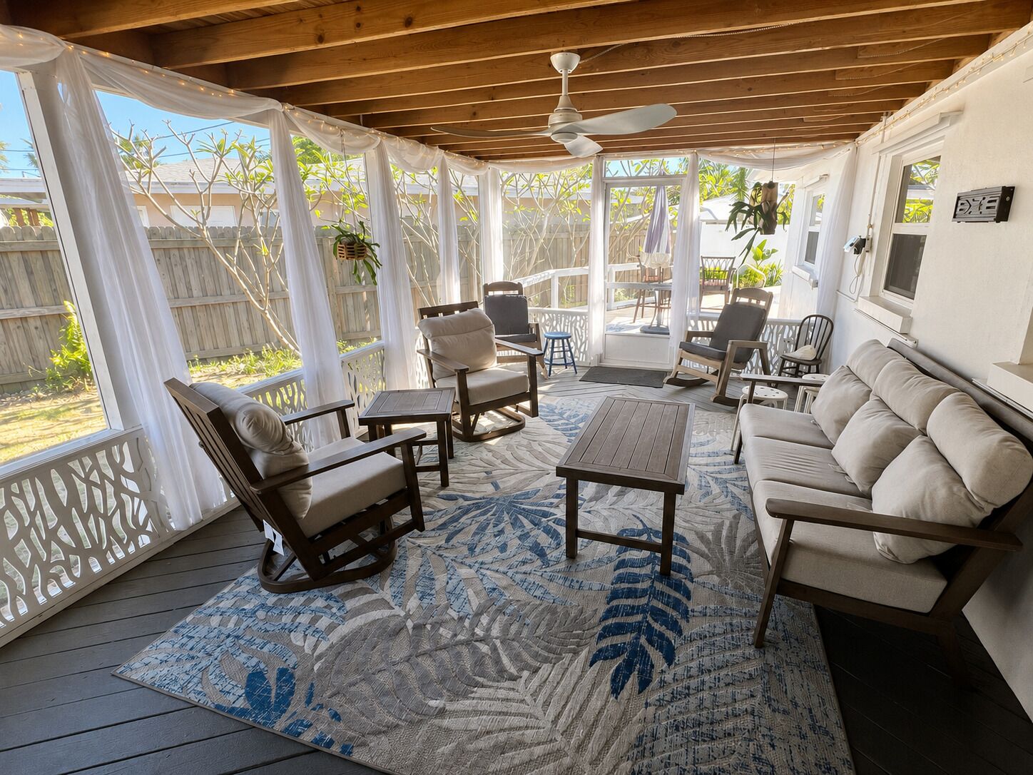 A covered outdoor seating area with a ceiling fan, wooden furniture, and a patterned rug.