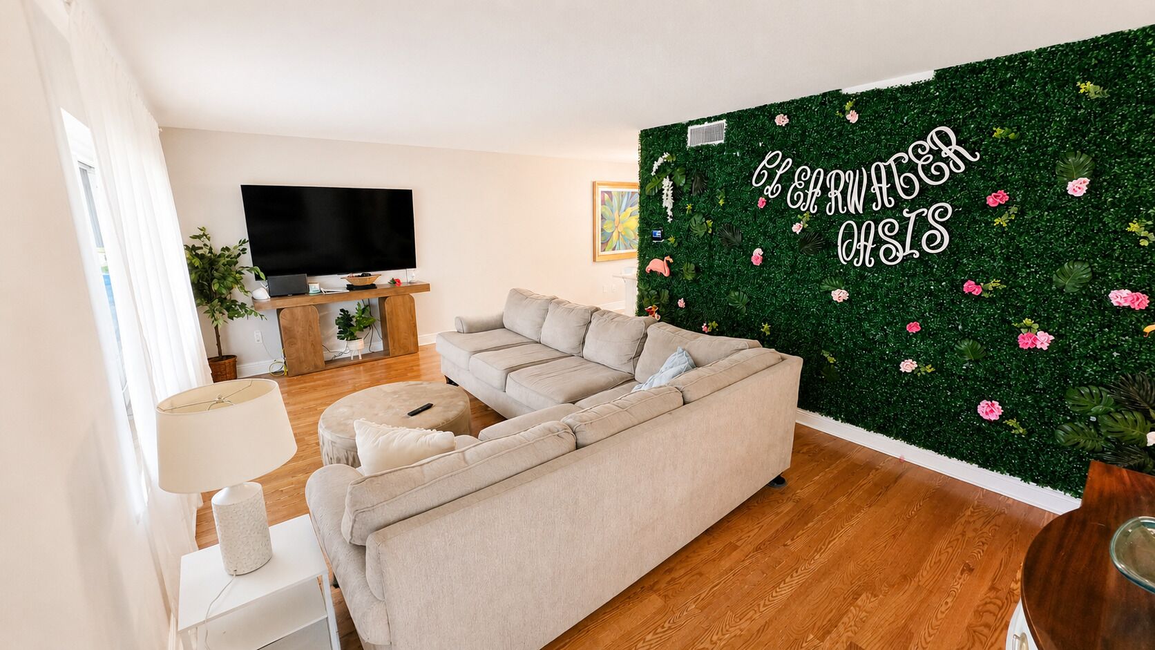 Een woonkamer met een bank, een televisie, een lamp en een groene muur met een bloemendecor.