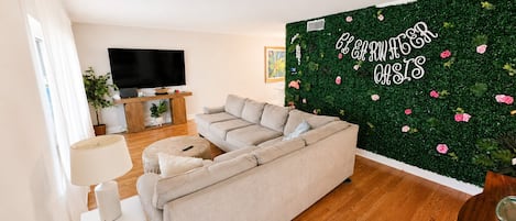 Un salon avec un canapé, un téléviseur, une lampe et un mur vert orné d’un motif floral.