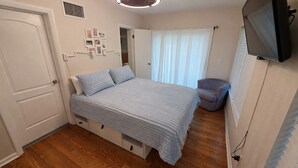 Ein Schlafzimmer mit einem Bett, einem Sessel, einem Fernseher und einer Tür.