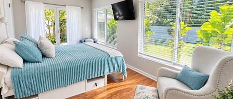 Une chambre à coucher avec un lit, une chaise, un téléviseur et une fenêtre avec des stores.