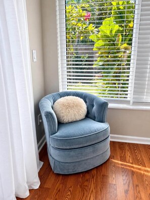 Una habitación en esquina con un sillón azul, un cojín mullido, una ventana con persianas y suelo de madera.