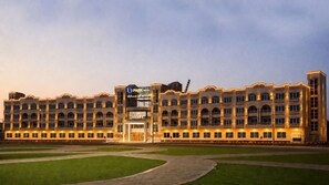 A multi-story hotel with a central entrance, balconies, and a well-maintained lawn.