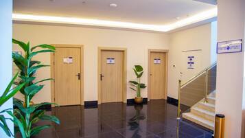 Un vestíbulo de hotel con piso pulido, tres puertas de madera, una escalera y plantas en macetas.