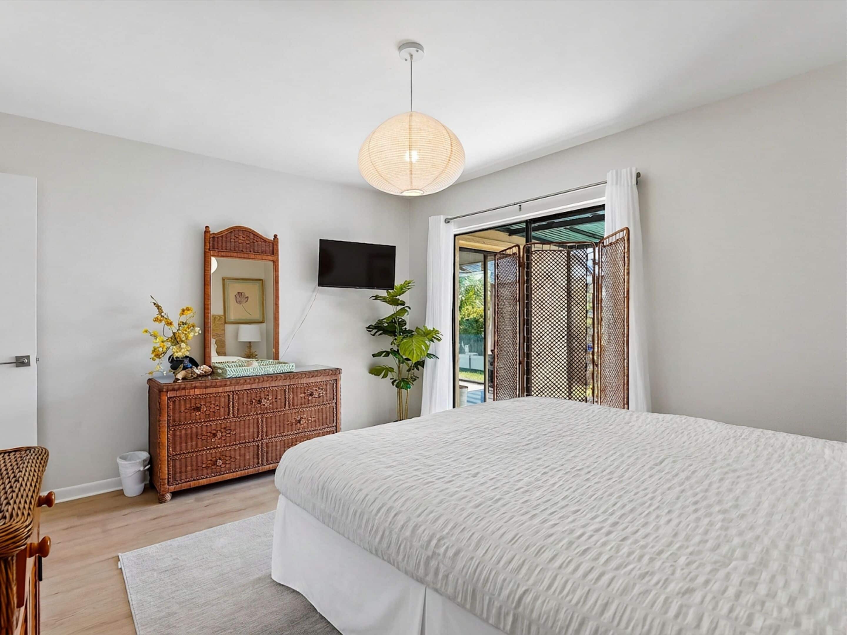 Een slaapkamer met een groot bed, een dressoir, een televisie en een schuifdeur naar een balkon.