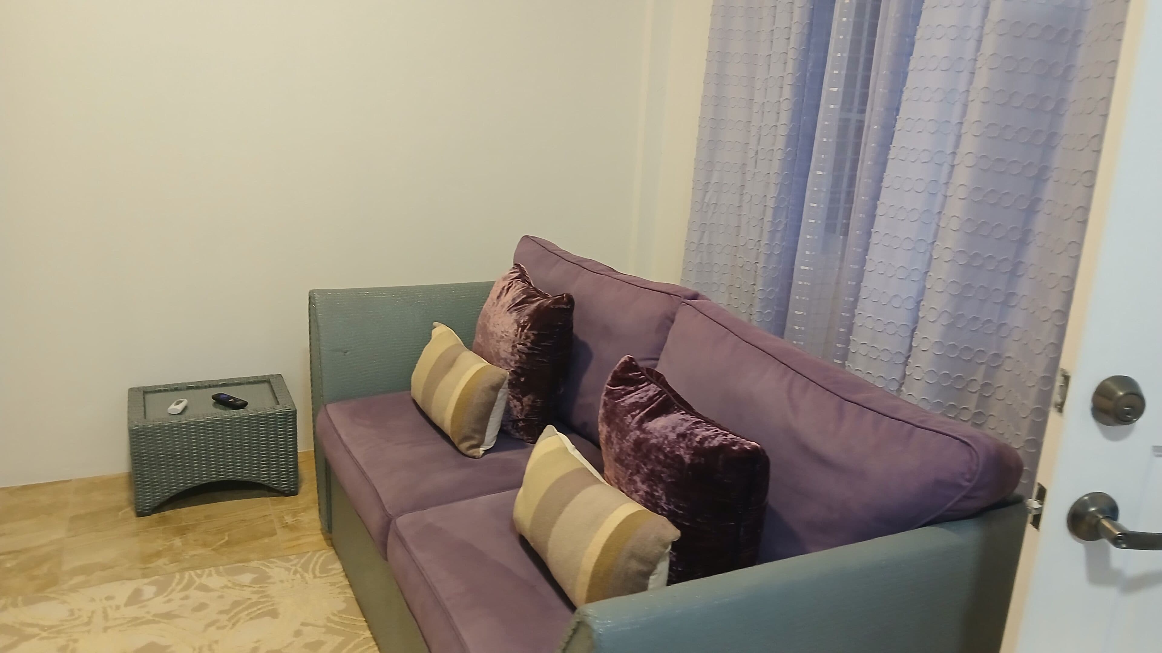 A room with a purple sofa, a small wicker side table, and a door with a metal handle.