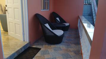 A hallway with a door, two black chairs with white cushions, and a tiled floor.