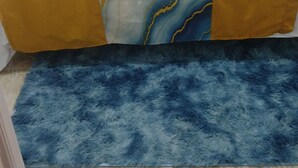 Una cama con una colcha estampada en amarillo y blanco, un manto suave de color azul y un piso de mármol.