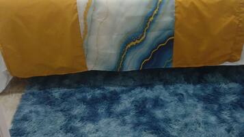 A bed with a yellow and white patterned bedspread, a blue fluffy rug, and a marble floor.