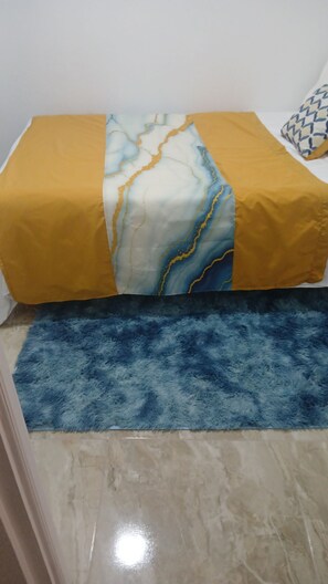 Ein Bett mit gelb-weißer Bettdecke, einem flauschigen blauen Teppich und einem Marmorboden.