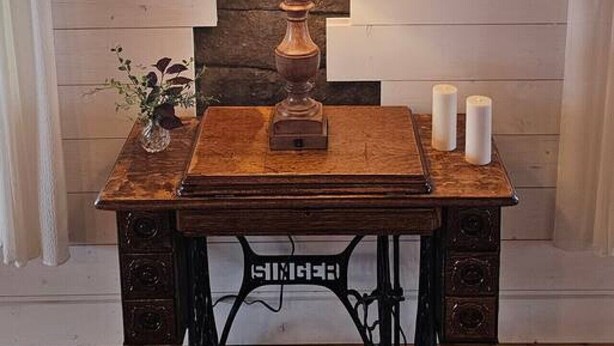 Une table en bois, ornée d’une lampe, de bougies et d’un vase rempli de fleurs, placée devant un mur orné d’un motif géométrique.