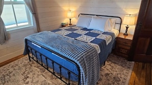 Une chambre avec un lit, deux lampes de chevet, une fenêtre avec des rideaux et un tapis à motifs.
