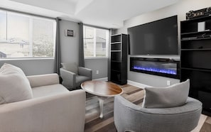 A modern living room with a fireplace, grey sofas, a coffee table, and a TV mounted on the wall. - Huge Yard Pet Friendly 2-bedroom Garden Level Private Suite with Kitchen (Thornton)
