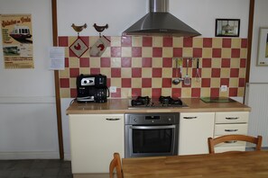 A kitchen with a stove, oven, and coffee maker. There are two chairs and a table.