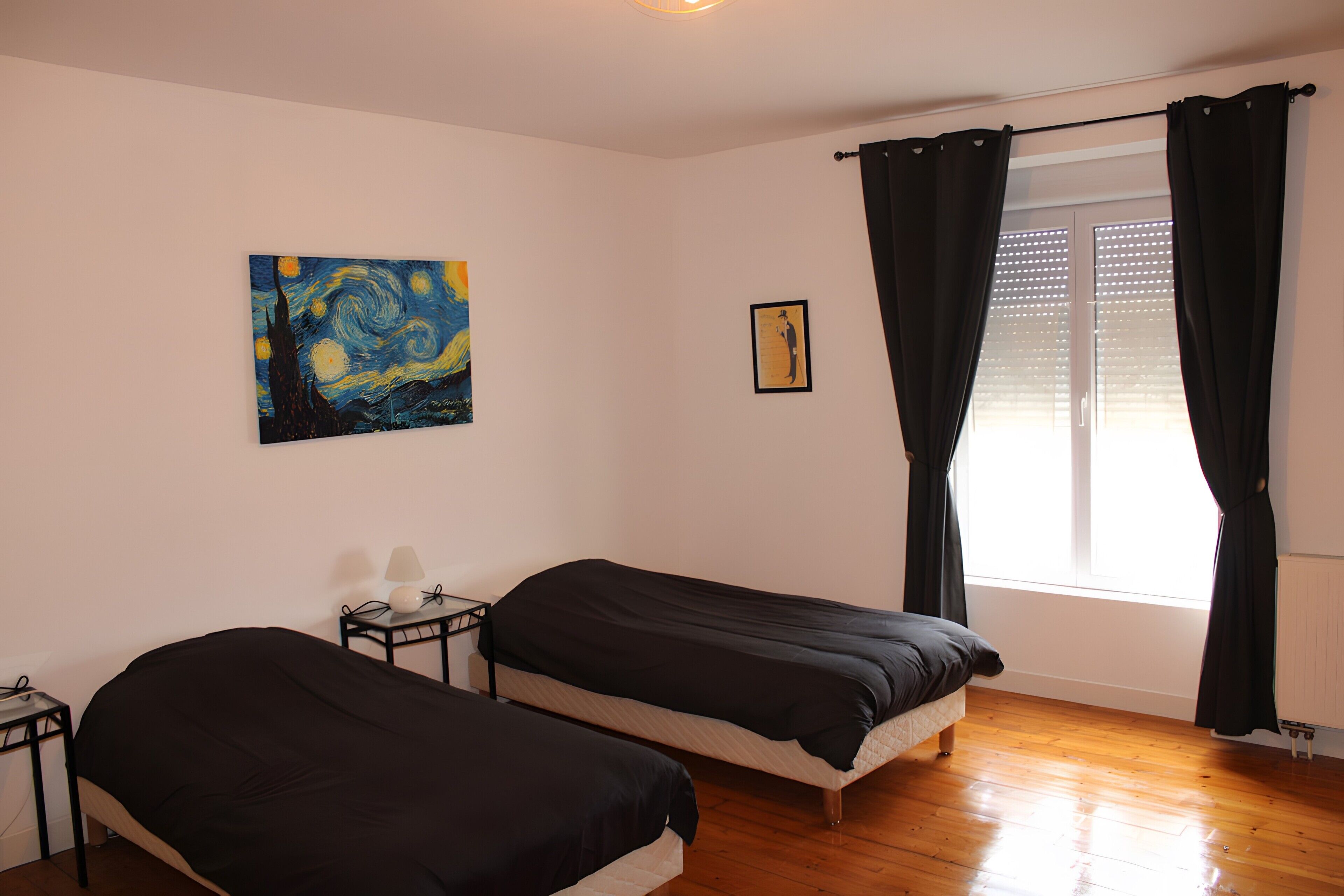 Een kamer met twee bedden, een schilderij aan de muur, een tafeltje met een lamp en een raam met gordijnen.