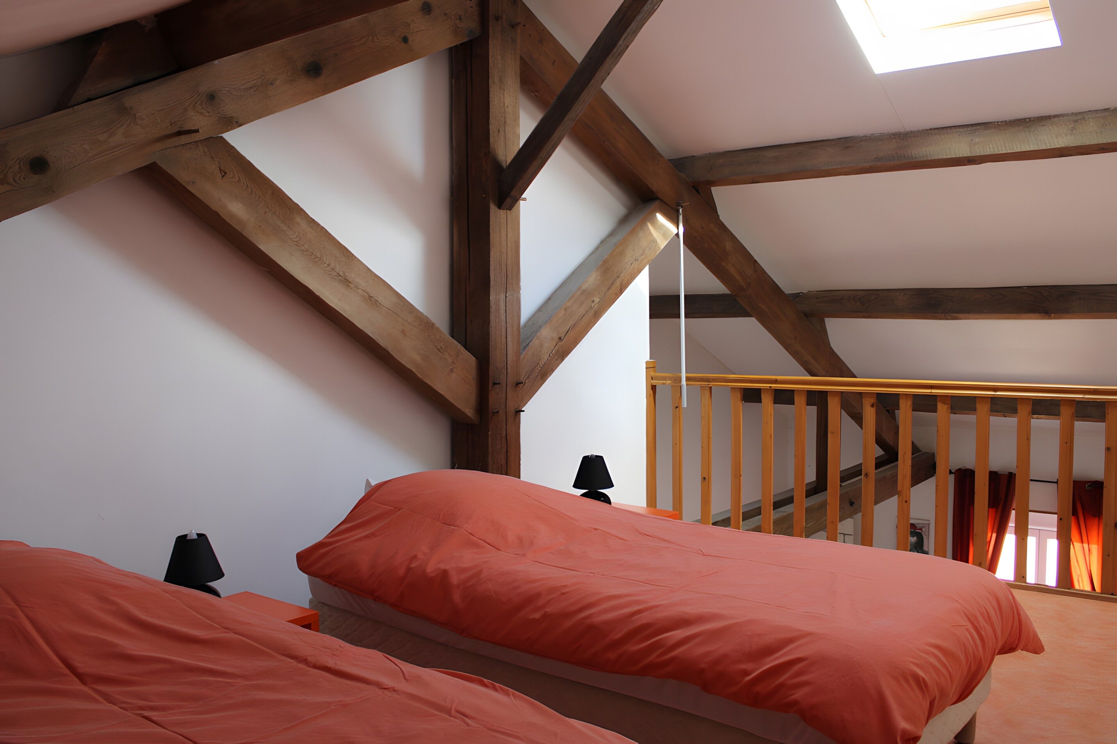 Quarto com duas camas, vigas de madeira, claraboia e escada.