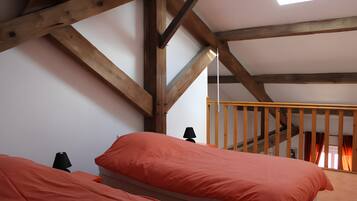 Quarto com duas camas, vigas de madeira, claraboia e escada.