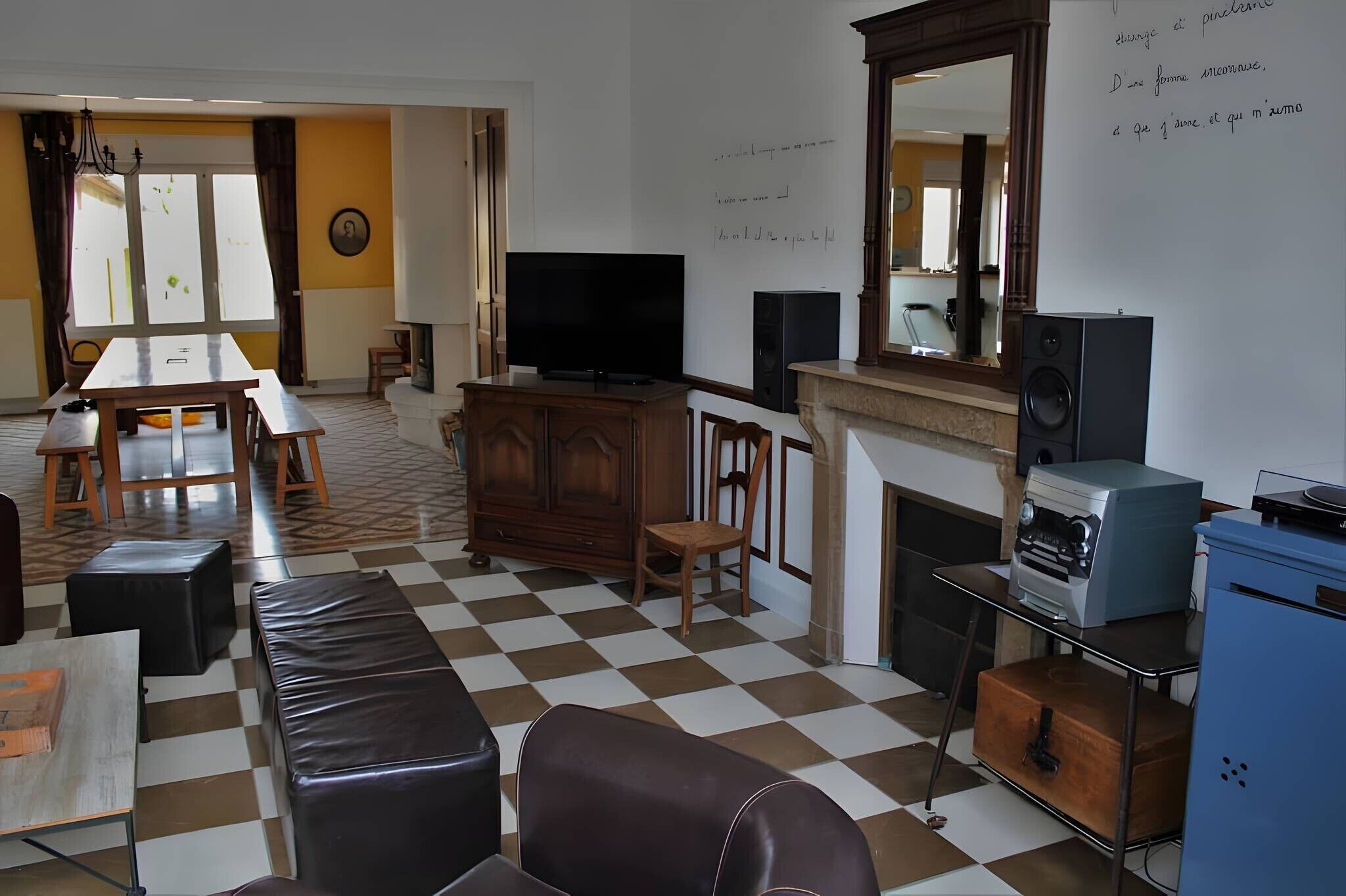 A living room with a checkered floor, a television, a fireplace, and a dining area with a table and chairs.