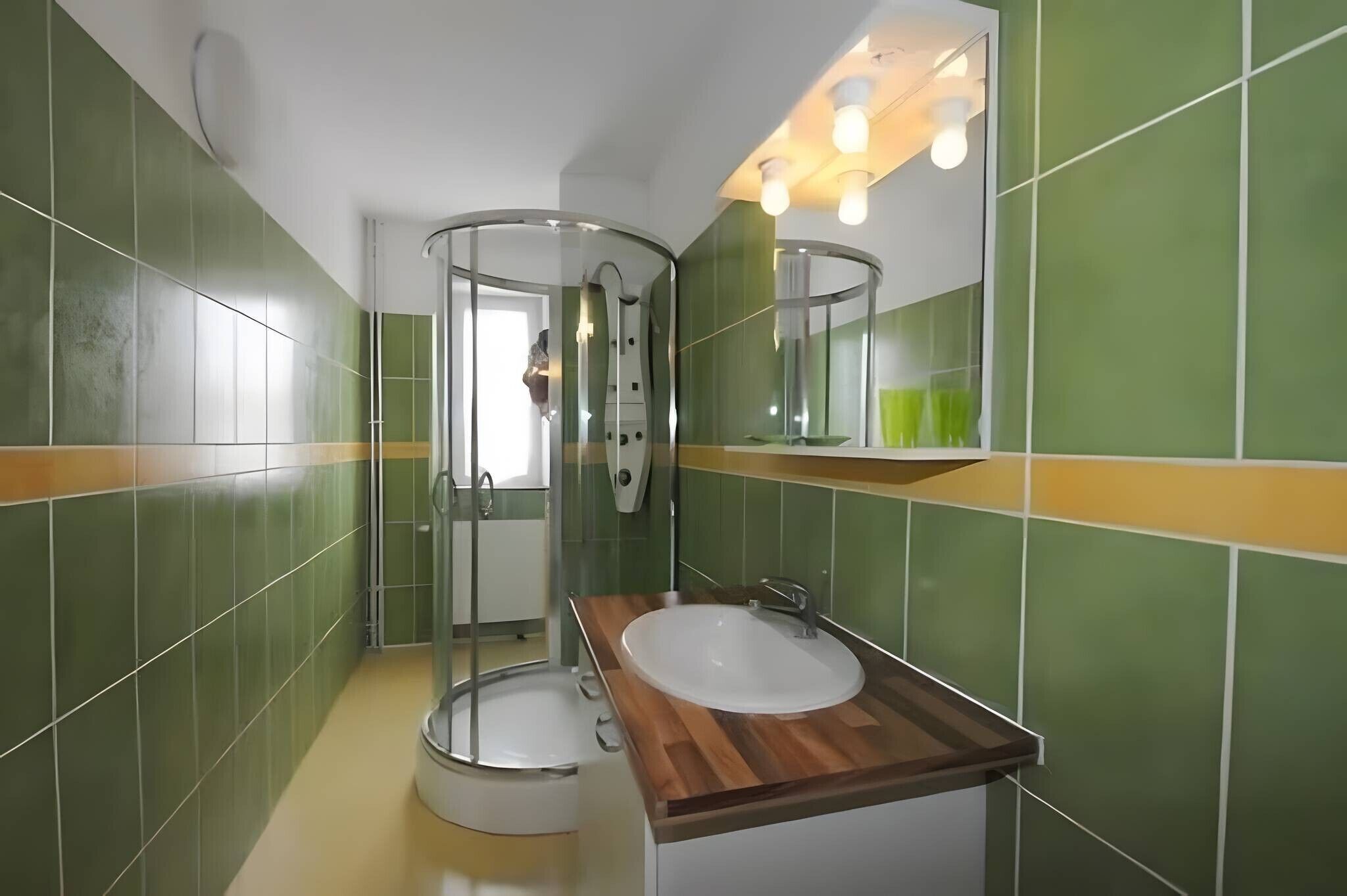 Une salle de bain avec une douche à parois de verre, un meuble-lavabo en bois et des murs recouverts de carreaux verts.