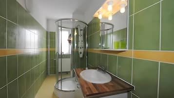 Une salle de bain avec une douche à parois de verre, un meuble-lavabo en bois et des murs recouverts de carreaux verts.
