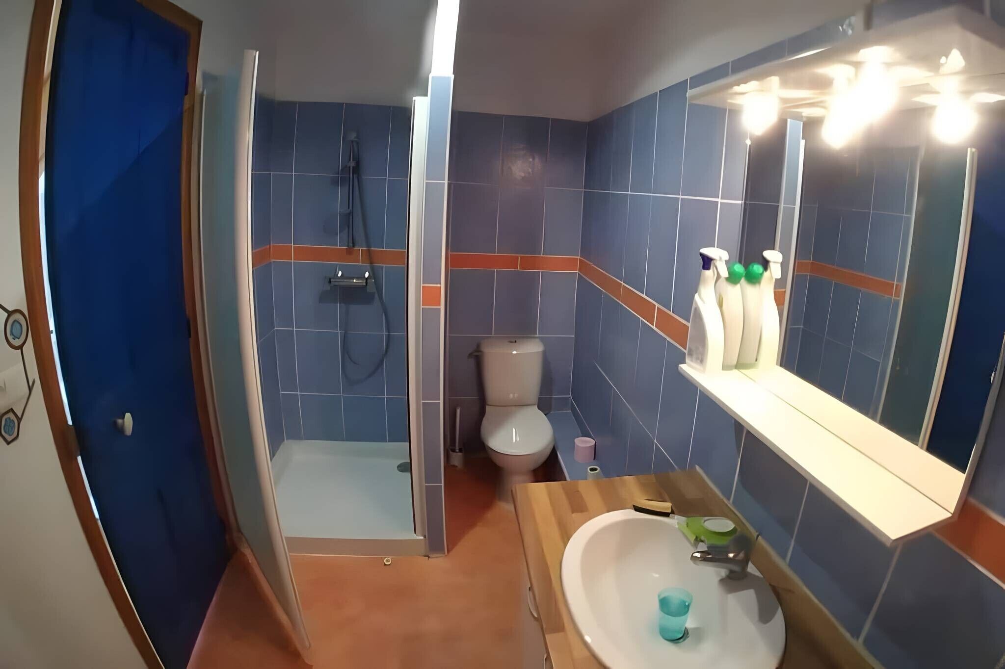 A bathroom with a shower, toilet, sink, and a mirror with lights.