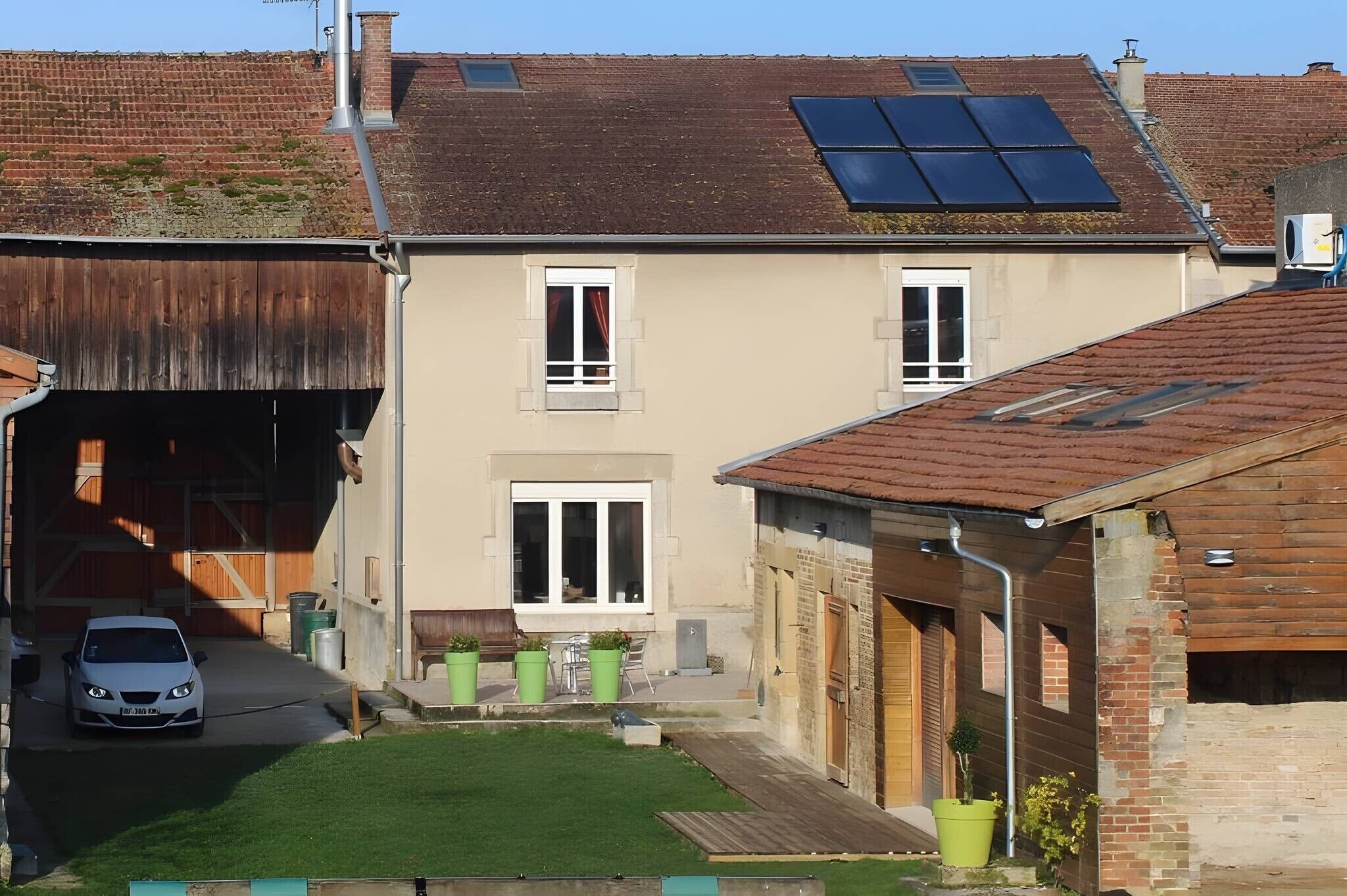 A residential property with a car parked in the driveway, a small lawn, and a solar panel on the roof.