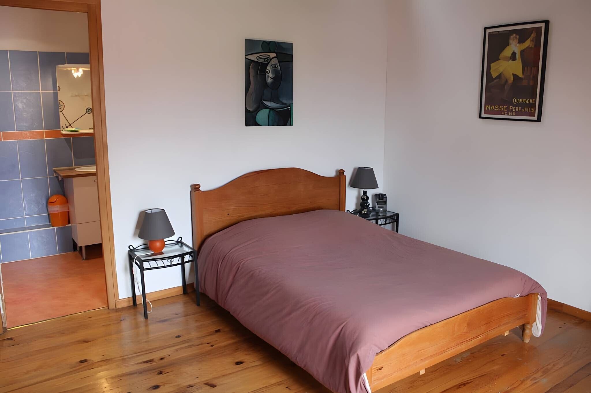 A bedroom with a wooden bed, a nightstand with a lamp, a wall art piece, and a poster.