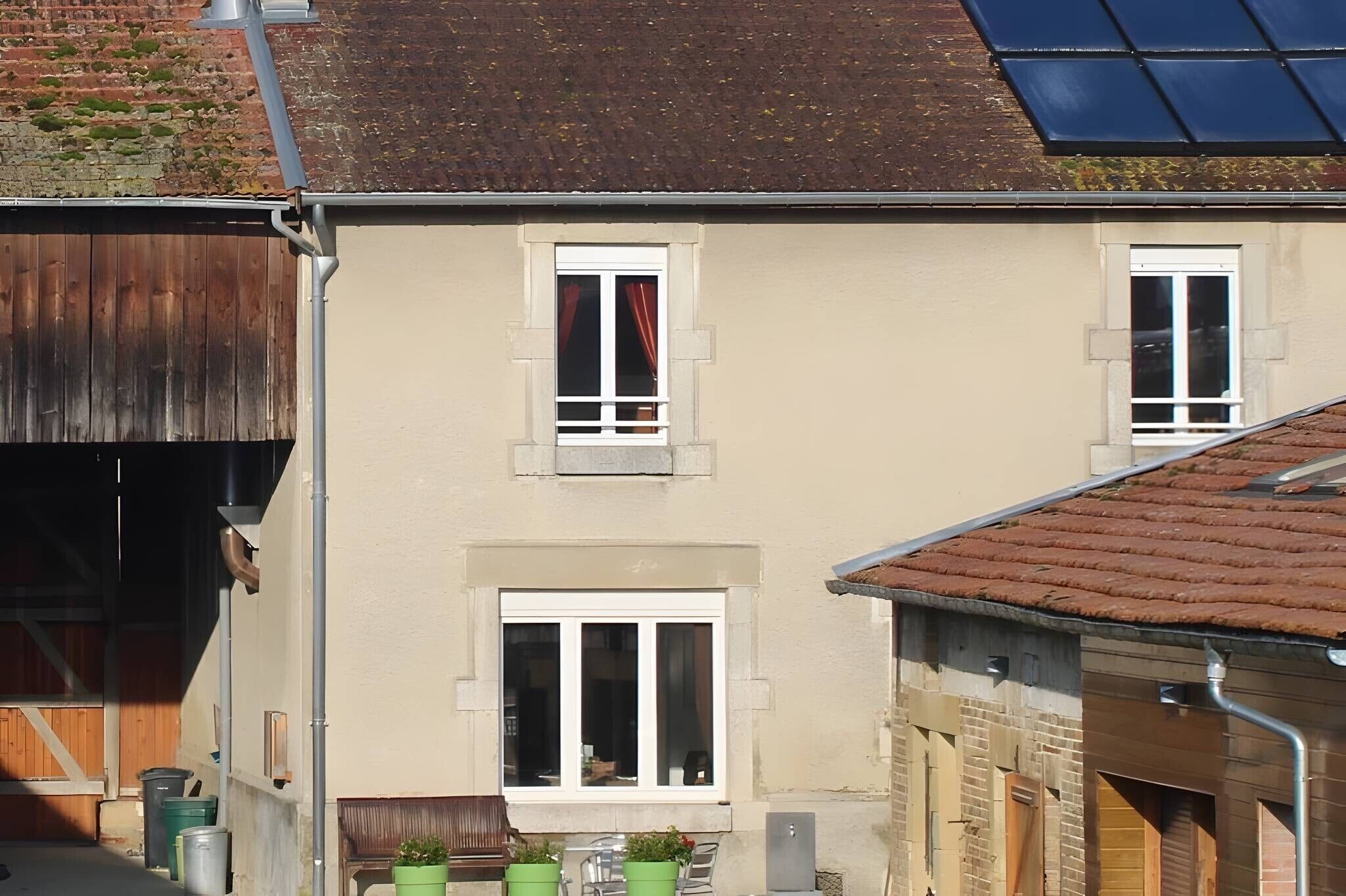 Un bâtiment à deux étages, doté d’un toit plat, d’un petit porche à l’avant avec un banc et d’une fenêtre ornée d’un rideau rouge.