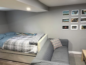 A room with a bed, a grey sofa, and a wall with framed pictures.