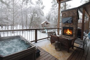 A deck with a hot tub, outdoor seating, and a stone fireplace. - Spotted Feather: Escape and enjoy Hot Tub, Playset, Foosball, and Fireplaces. (Broken Bow)
