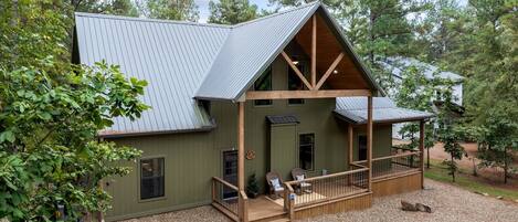 A two-story cabin with a porch, surrounded by trees.