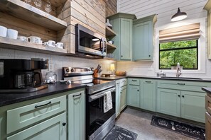 A kitchen with a built-in oven, a coffee maker, and a window with a view of greenery. - Spotted Feather: Escape and enjoy Hot Tub, Playset, Foosball, and Fireplaces. (Broken Bow)