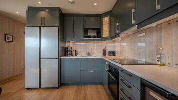 A modern kitchen with grey cabinets, a stainless steel refrigerator, and a wooden floor.