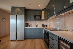 A modern kitchen with grey cabinets, a stainless steel refrigerator, and a wooden floor.